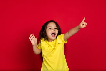 Image showing Beautiful emotional little girl isolated on red background. Half-lenght portrait of happy child gesturing