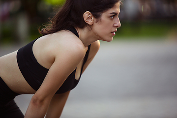 Image showing Young female athlete training in the city street in summer sunshine. Beautiful woman practicing, working out. Concept of sport, healthy lifestyle, movement, activity.