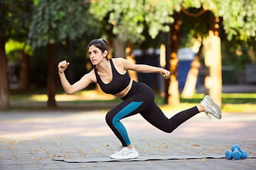 Image showing Young female athlete training in the city street in summer sunshine. Beautiful woman practicing, working out. Concept of sport, healthy lifestyle, movement, activity.