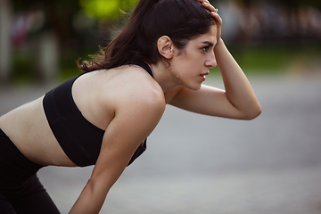 Image showing Young female athlete training in the city street in summer sunshine. Beautiful woman practicing, working out. Concept of sport, healthy lifestyle, movement, activity.