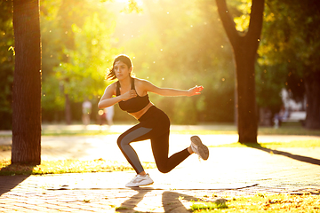 Image showing Young female athlete training in the city street in summer sunshine. Beautiful woman practicing, working out. Concept of sport, healthy lifestyle, movement, activity.