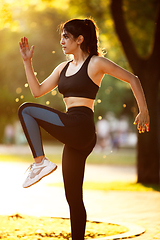 Image showing Young female athlete training in the city street in summer sunshine. Beautiful woman practicing, working out. Concept of sport, healthy lifestyle, movement, activity.