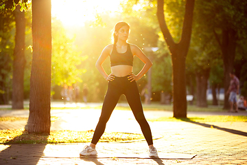 Image showing Young female athlete training in the city street in summer sunshine. Beautiful woman practicing, working out. Concept of sport, healthy lifestyle, movement, activity.