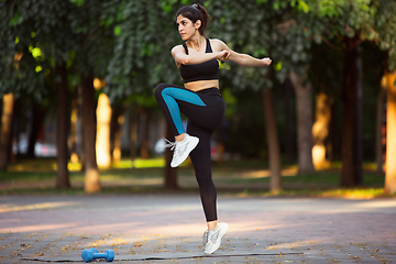 Image showing Young female athlete training in the city street in summer sunshine. Beautiful woman practicing, working out. Concept of sport, healthy lifestyle, movement, activity.