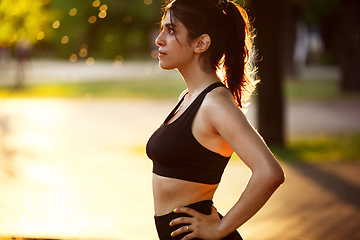 Image showing Young female athlete training in the city street in summer sunshine. Beautiful woman practicing, working out. Concept of sport, healthy lifestyle, movement, activity.