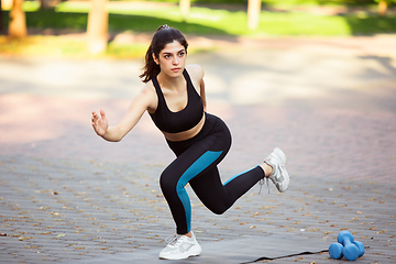 Image showing Young female athlete training in the city street in summer sunshine. Beautiful woman practicing, working out. Concept of sport, healthy lifestyle, movement, activity.