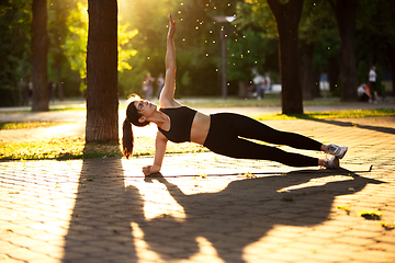 Image showing Young female athlete training in the city street in summer sunshine. Beautiful woman practicing, working out. Concept of sport, healthy lifestyle, movement, activity.