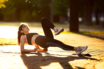 Image showing Young female athlete training in the city street in summer sunshine. Beautiful woman practicing, working out. Concept of sport, healthy lifestyle, movement, activity.