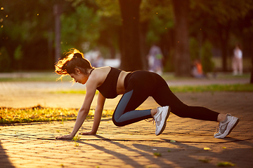 Image showing Young female athlete training in the city street in summer sunshine. Beautiful woman practicing, working out. Concept of sport, healthy lifestyle, movement, activity.