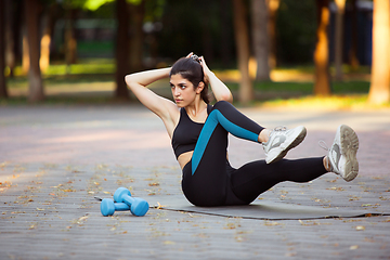 Image showing Young female athlete training in the city street in summer sunshine. Beautiful woman practicing, working out. Concept of sport, healthy lifestyle, movement, activity.