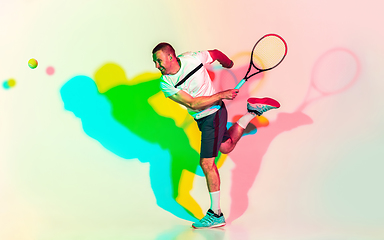 Image showing Caucasian male professional sportsman playing tennis on studio background in neon light