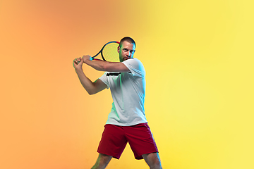 Image showing Caucasian male professional sportsman playing tennis on studio background in neon light