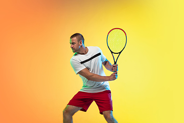 Image showing Caucasian male professional sportsman playing tennis on studio background in neon light