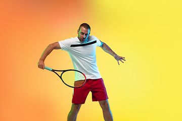 Image showing Caucasian male professional sportsman playing tennis on studio background in neon light