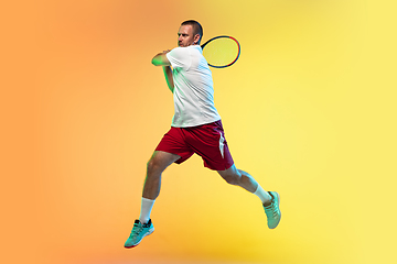 Image showing Caucasian male professional sportsman playing tennis on studio background in neon light