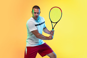 Image showing Caucasian male professional sportsman playing tennis on studio background in neon light