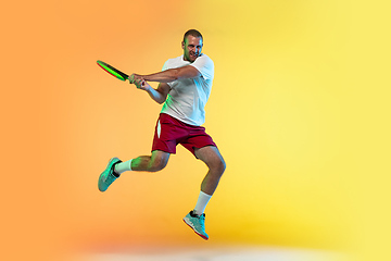 Image showing Caucasian male professional sportsman playing tennis on studio background in neon light