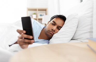 Image showing sleepy indian man with smartphone lying in bed