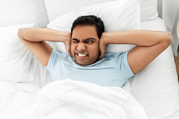 Image showing annoyed indian man lying in bed and closing ears