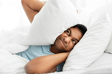 Image showing annoyed indian man lying in bed and closing ears