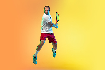 Image showing Caucasian male professional sportsman playing tennis on studio background in neon light