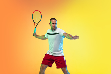 Image showing Caucasian male professional sportsman playing tennis on studio background in neon light