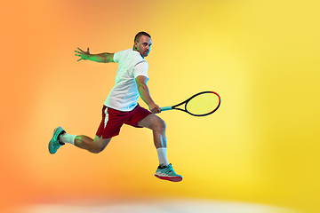 Image showing Caucasian male professional sportsman playing tennis on studio background in neon light