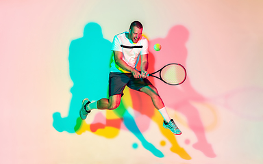 Image showing Caucasian male professional sportsman playing tennis on studio background in neon light