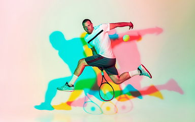 Image showing Caucasian male professional sportsman playing tennis on studio background in neon light