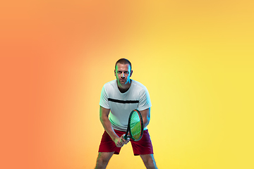 Image showing Caucasian male professional sportsman playing tennis on studio background in neon light