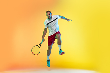 Image showing Caucasian male professional sportsman playing tennis on studio background in neon light