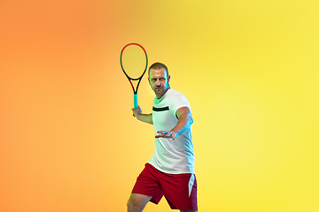 Image showing Caucasian male professional sportsman playing tennis on studio background in neon light