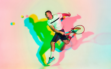 Image showing Caucasian male professional sportsman playing tennis on studio background in neon light