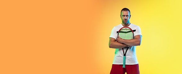 Image showing Caucasian male professional sportsman playing tennis on studio background in neon light