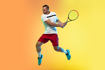 Image showing Caucasian male professional sportsman playing tennis on studio background in neon light