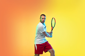 Image showing Caucasian male professional sportsman playing tennis on studio background in neon light