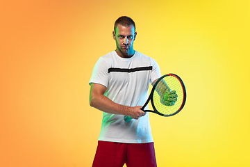 Image showing Caucasian male professional sportsman playing tennis on studio background in neon light