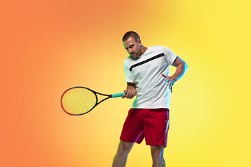 Image showing Caucasian male professional sportsman playing tennis on studio background in neon light