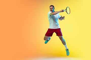 Image showing Caucasian male professional sportsman playing tennis on studio background in neon light