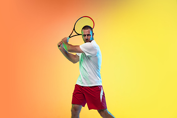 Image showing Caucasian male professional sportsman playing tennis on studio background in neon light