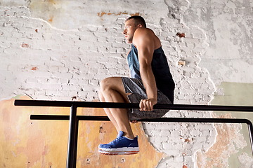 Image showing man flexing abs on parallel bars in gym