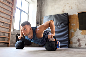 Image showing young man doing kettlebell push-ups in gym