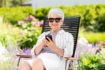 Image showing old woman with earphones and smartphone at garden