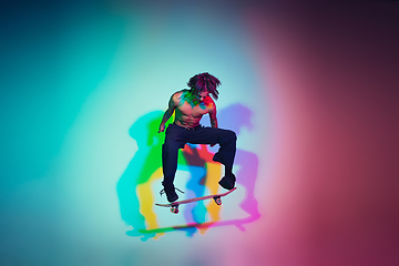 Image showing Skateboarder doing a trick isolated on studio background in colorful neon light