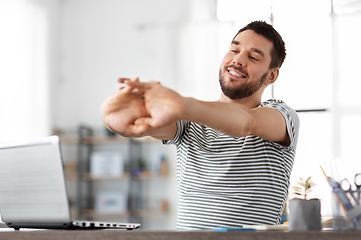 Image showing happy man with laptop stretching at home office