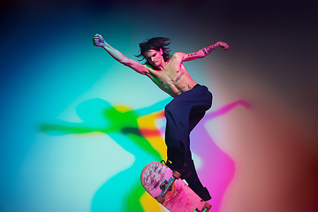 Image showing Skateboarder doing a trick isolated on studio background in colorful neon light