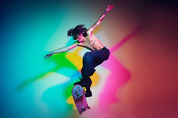 Image showing Skateboarder doing a trick isolated on studio background in colorful neon light