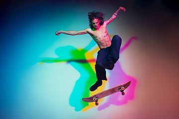 Image showing Skateboarder doing a trick isolated on studio background in colorful neon light