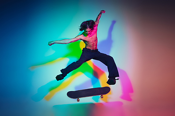 Image showing Skateboarder doing a trick isolated on studio background in colorful neon light