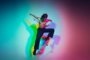 Image showing Skateboarder doing a trick isolated on studio background in colorful neon light